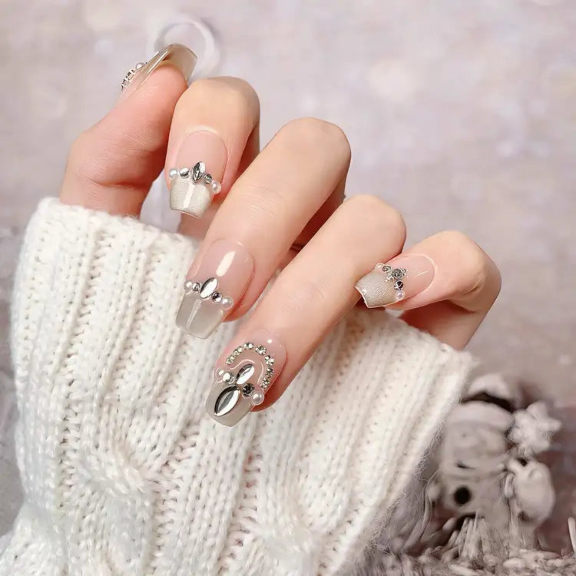 Close-up of a hand with decorative nails wearing a white knitted sweater.