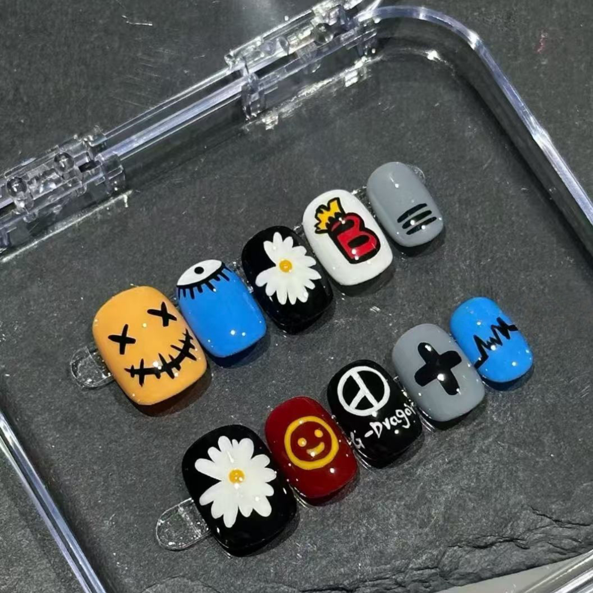 Set of colorful nail art designs in a clear case on a dark surface