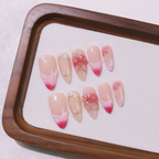Set of pink and red gradient nail art designs on a wooden tray with a white cloth background