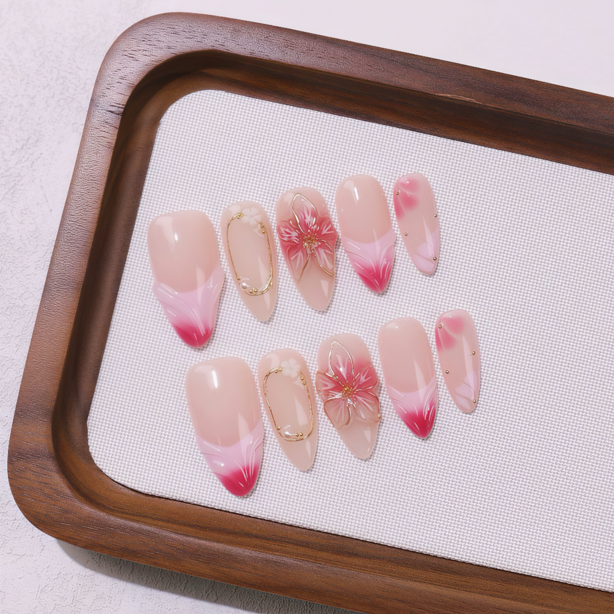 Set of pink and red gradient nail art designs on a wooden tray with a white cloth background