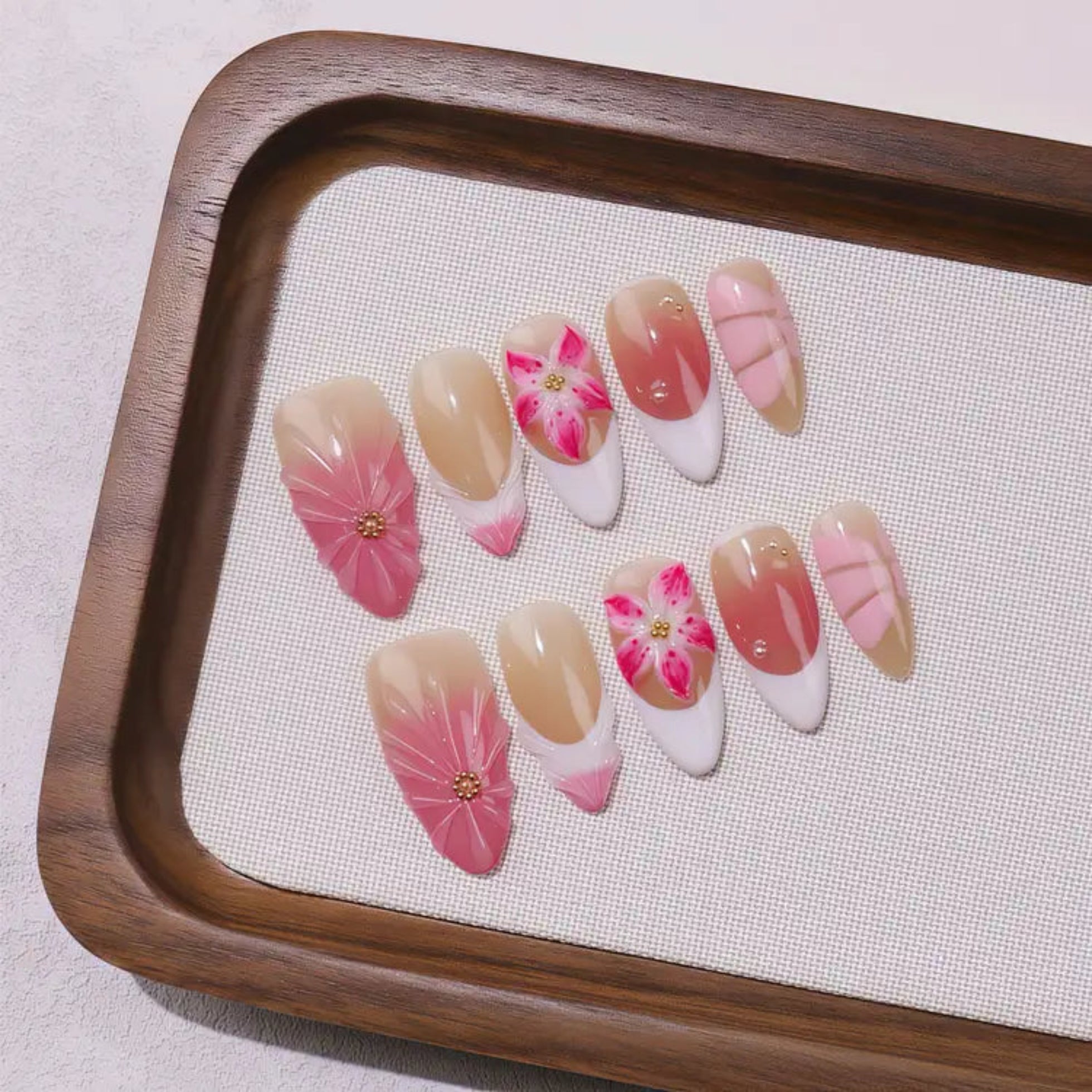 Nail art display with pink and beige flowers on a wooden tray