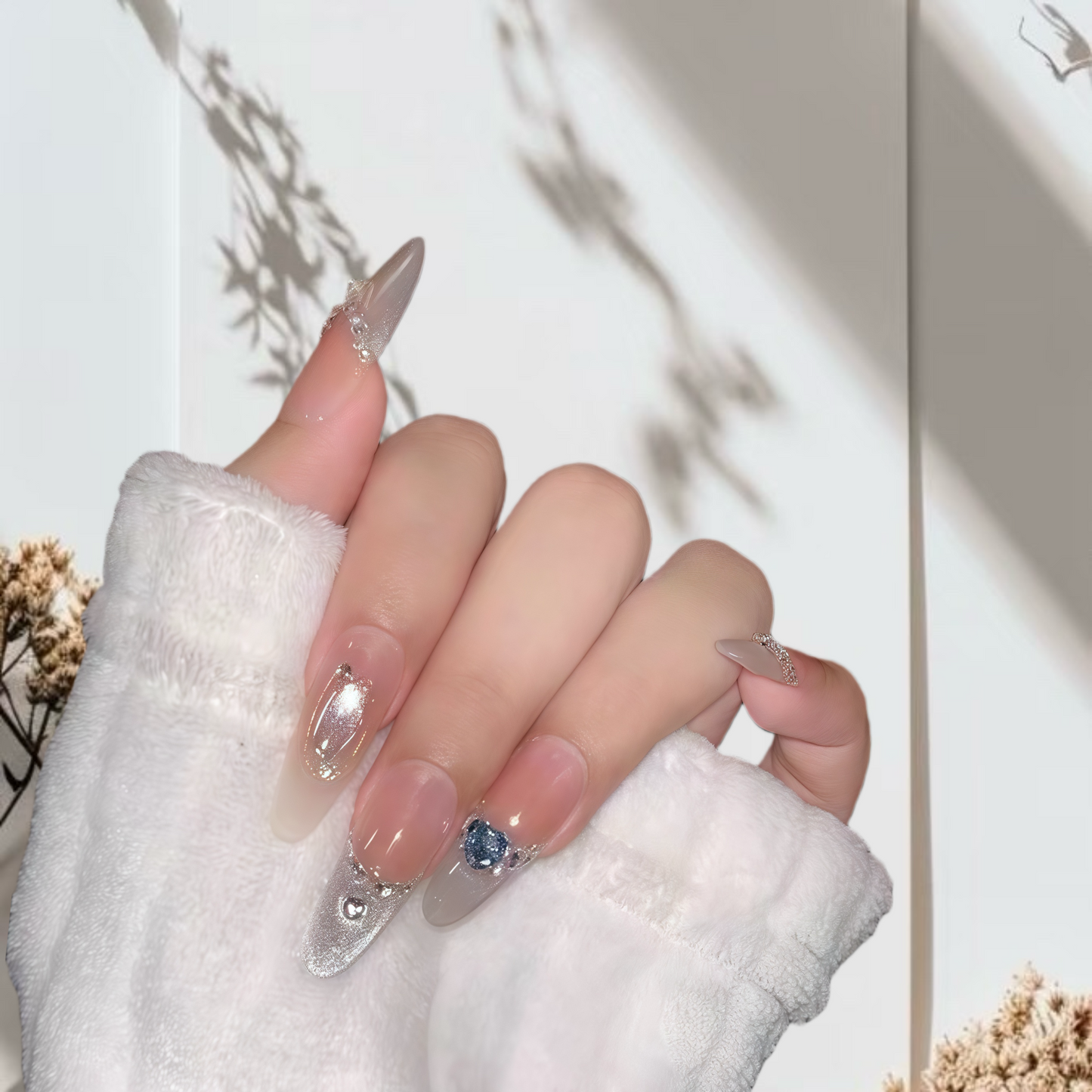 Hand with stylish nail design holding a small blue gemstone, against a neutral background.