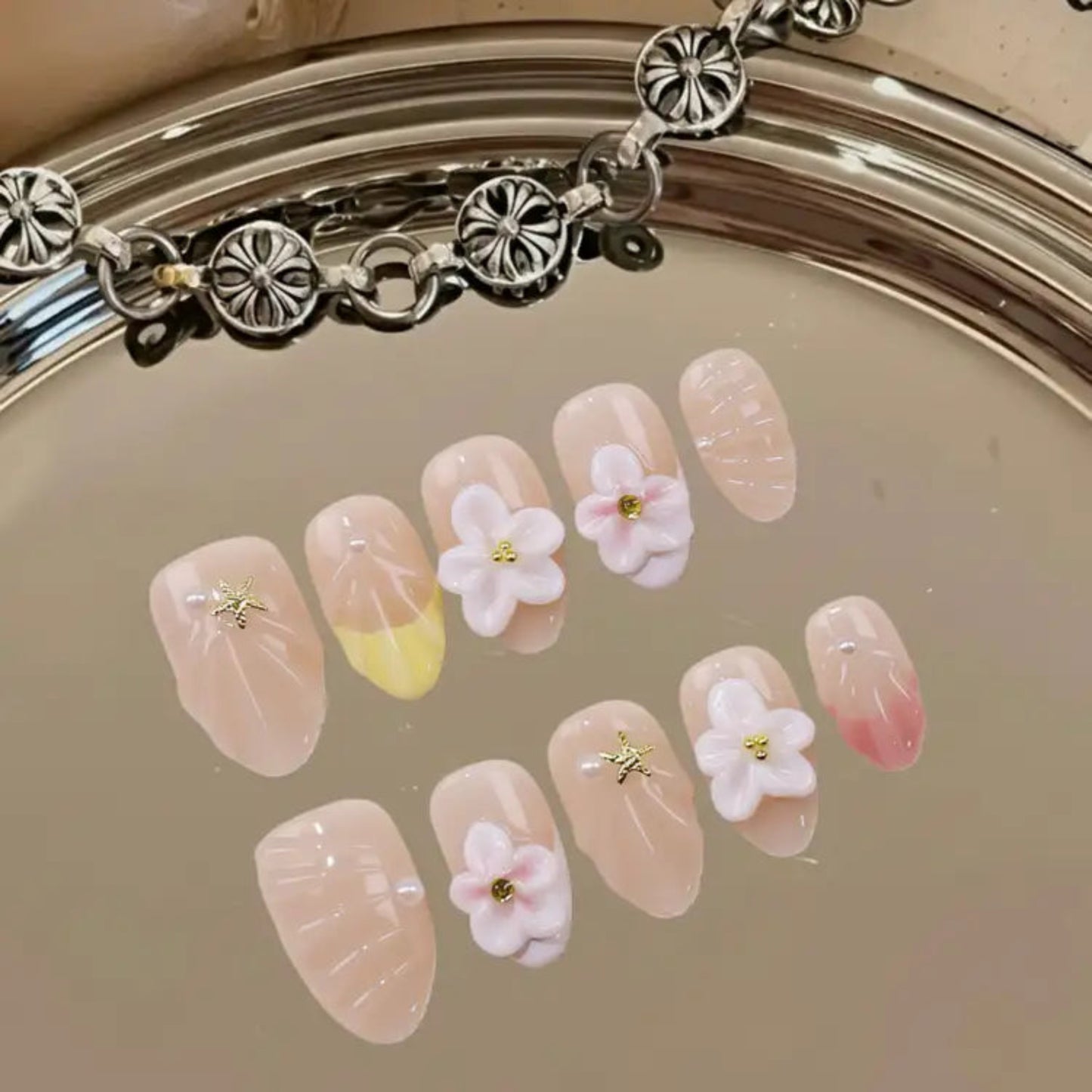 Decorative nail art with flowers and a bracelet on a reflective surface