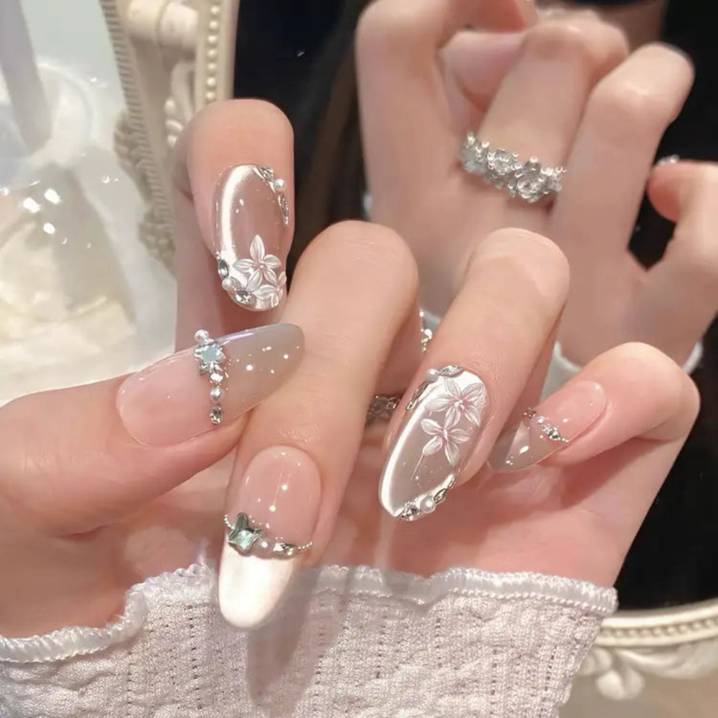 Close-up of hands with decorative nail art featuring flowers and rhinestones.