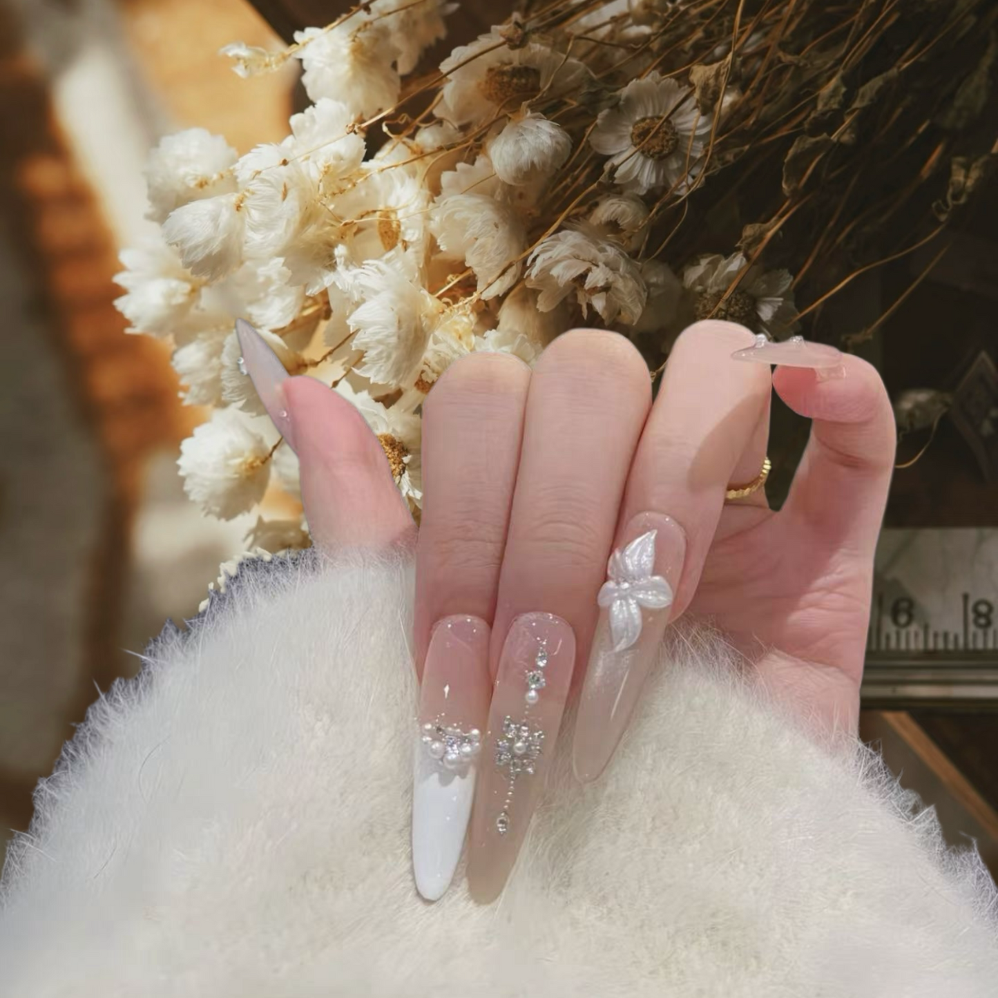 Close-up of a hand with decorative nails in front of white flowers