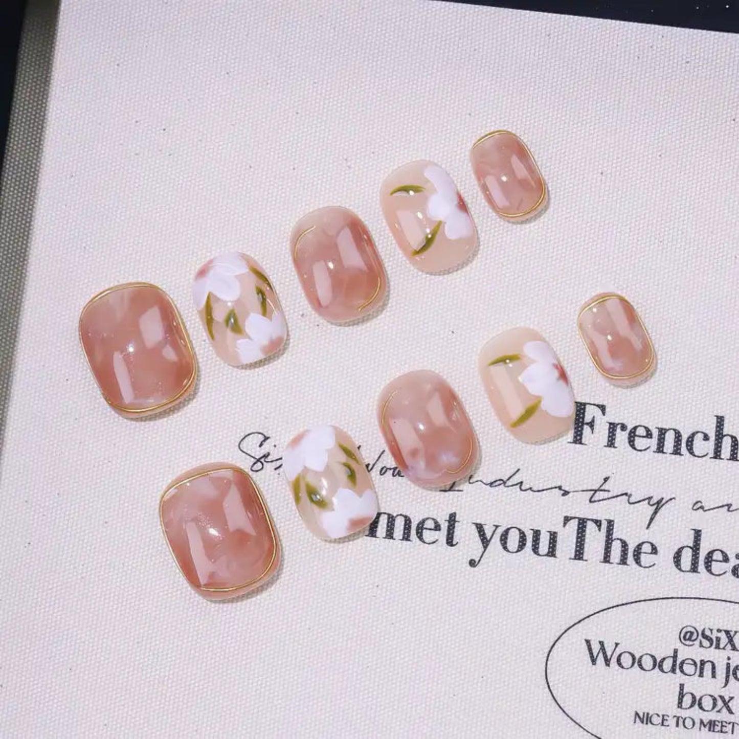 Set of pink and white floral nail art designs on a textured surface with text.