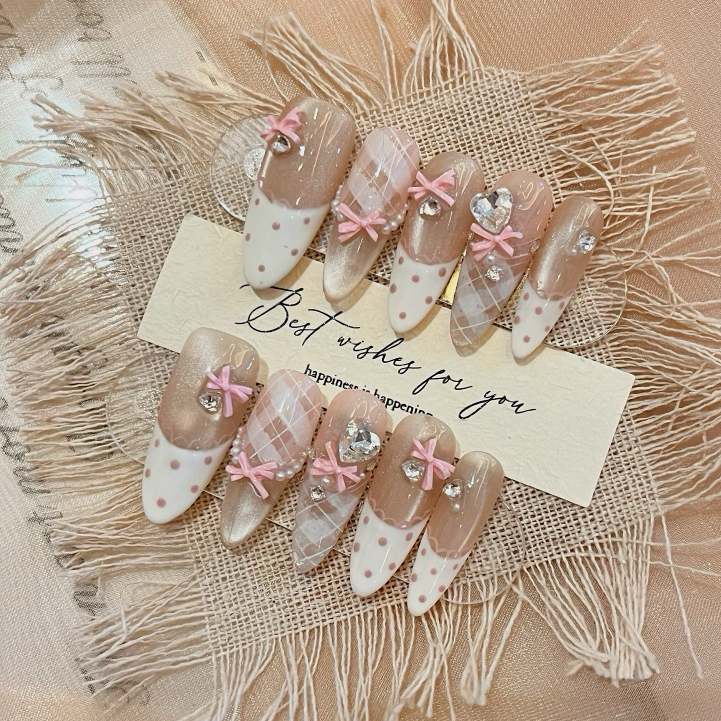 Decorative nails with pink bows and rhinestones on a textured surface with a card reading 'Best wishes for you'.