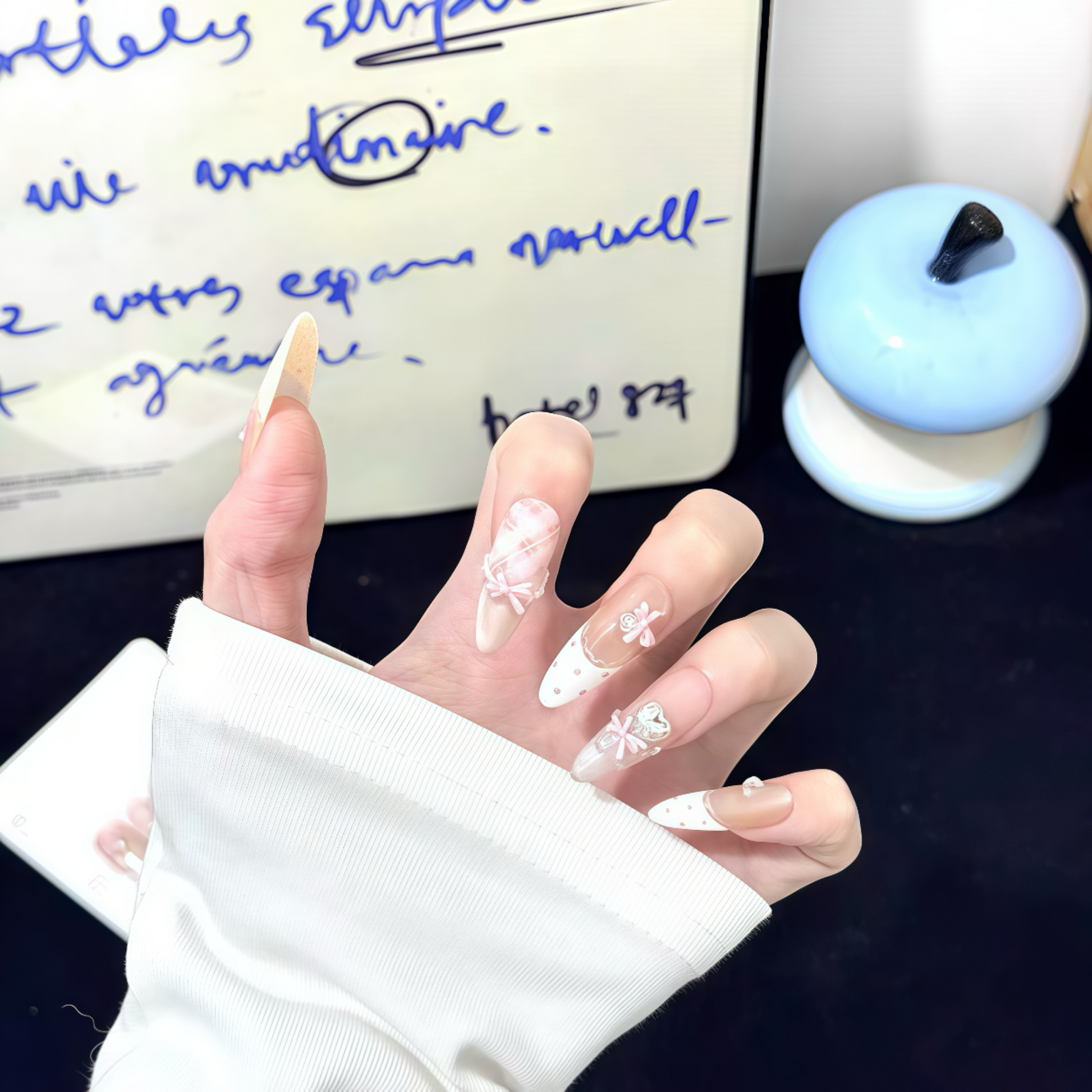 Hand with decorative nails in front of a handwritten letter on a desk.