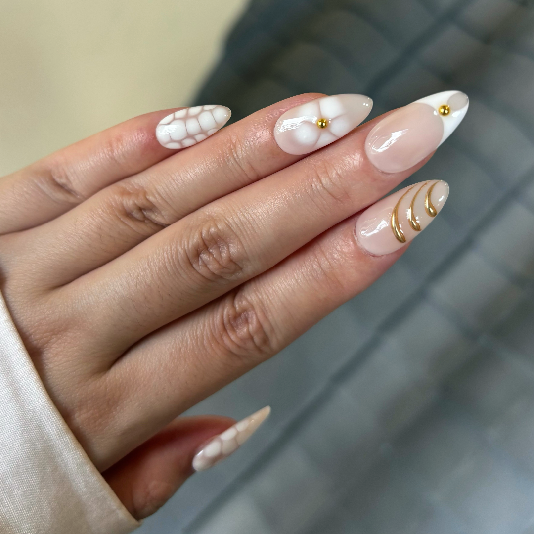 Hand with decorative nail art featuring white, gold, and pearl elements.