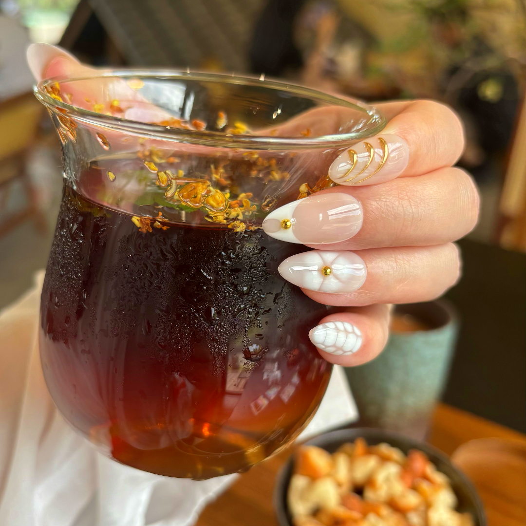 Hand holding a glass of dark liquid with floral nail design