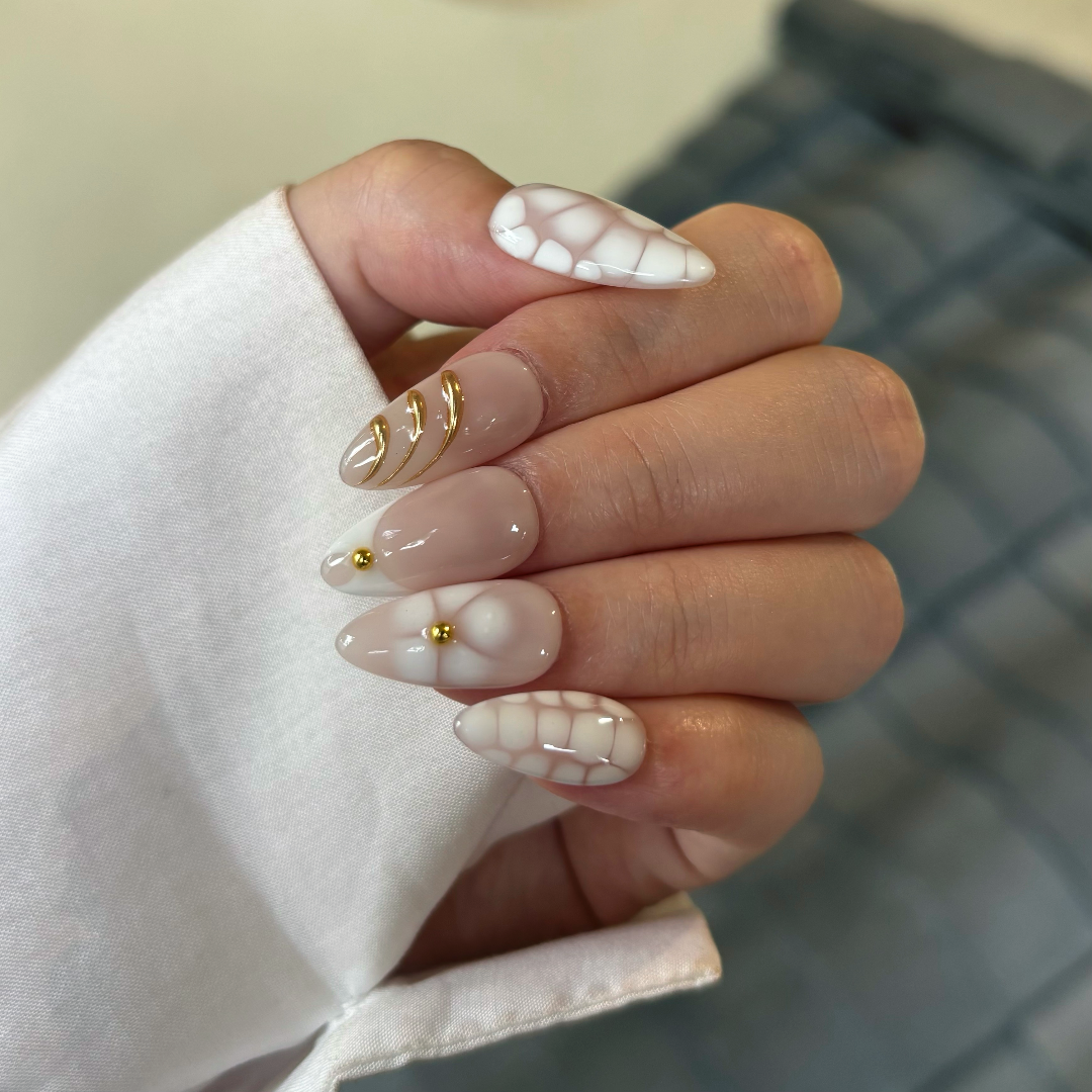 Hand with white nail polish and gold accents held by a person wearing a white shirt.
