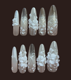 Set of decorative nail extensions with floral and geometric designs on a dark background