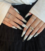 Close-up of hands with decorative nails and rings on a black background