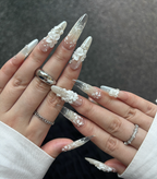 Close-up of hands with long, ornate nails featuring floral designs on a dark background.