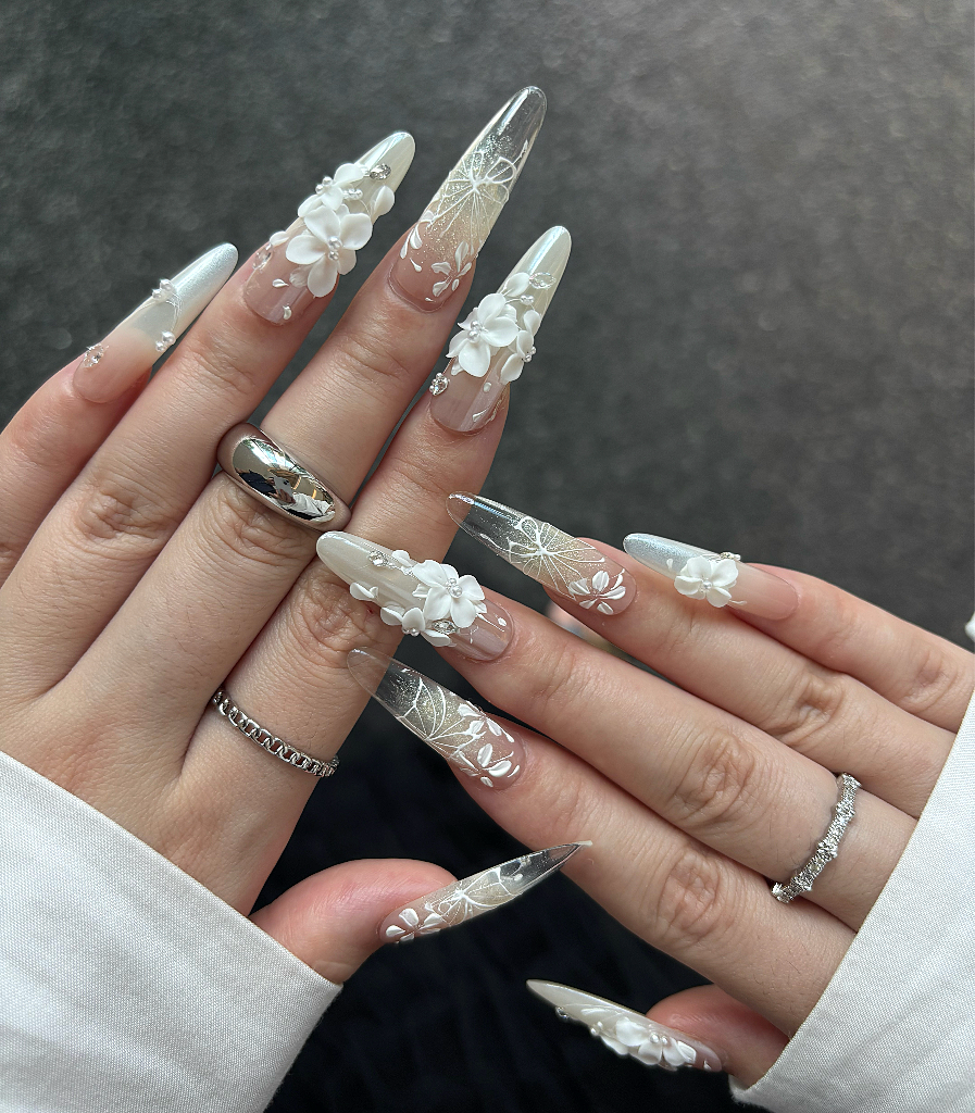 Close-up of hands with long, ornate nails featuring floral designs on a dark background.
