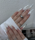 Close-up of hands with long, decorative nails and multiple rings on a neutral background
