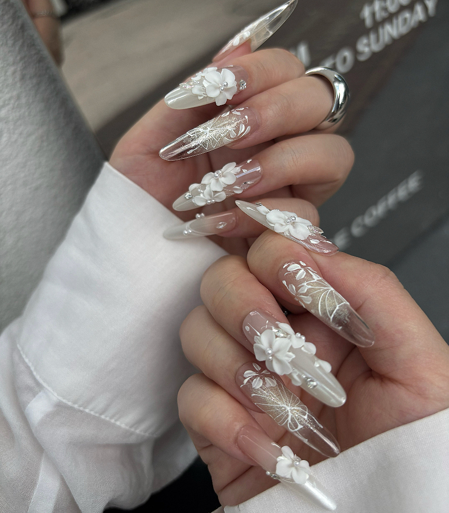 Close-up of hands with decorative floral nail art on clear gel base.