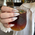 Hand holding a clear cup with iced coffee, wearing a white shirt.