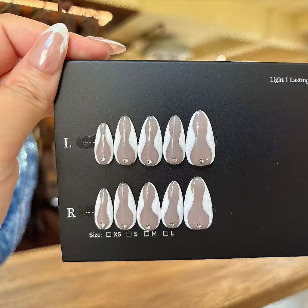 Set of nail extensions on a black card held by a hand with light nail polish.
