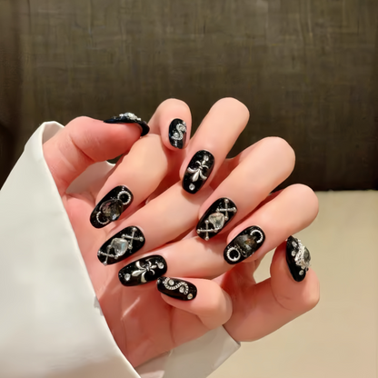 Hand with black nail art featuring white designs on a neutral background