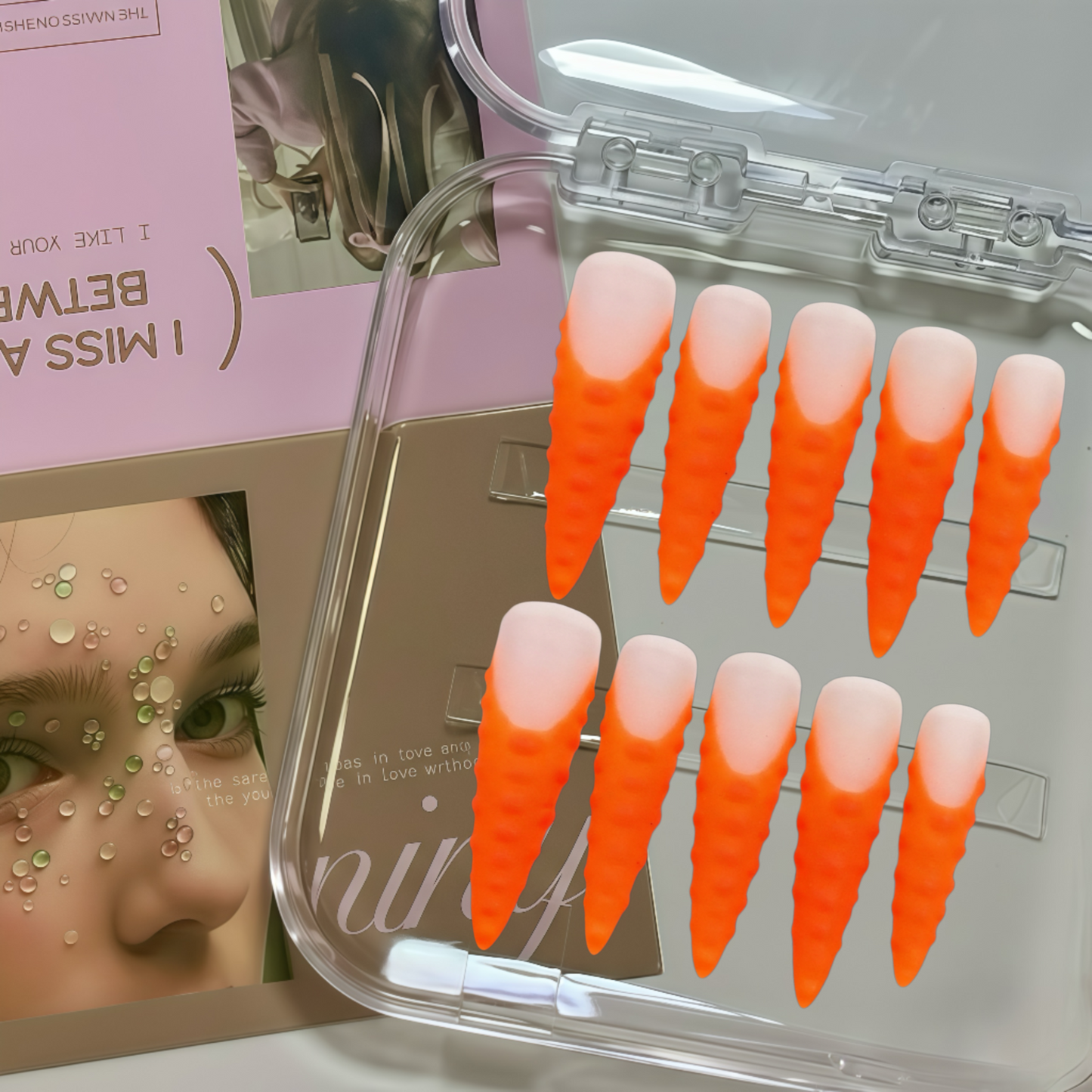 Set of orange and pink gradient false nails in a clear case with a magazine in the background.