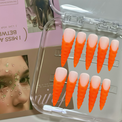 Set of orange and pink gradient false nails in a clear case with a magazine in the background.