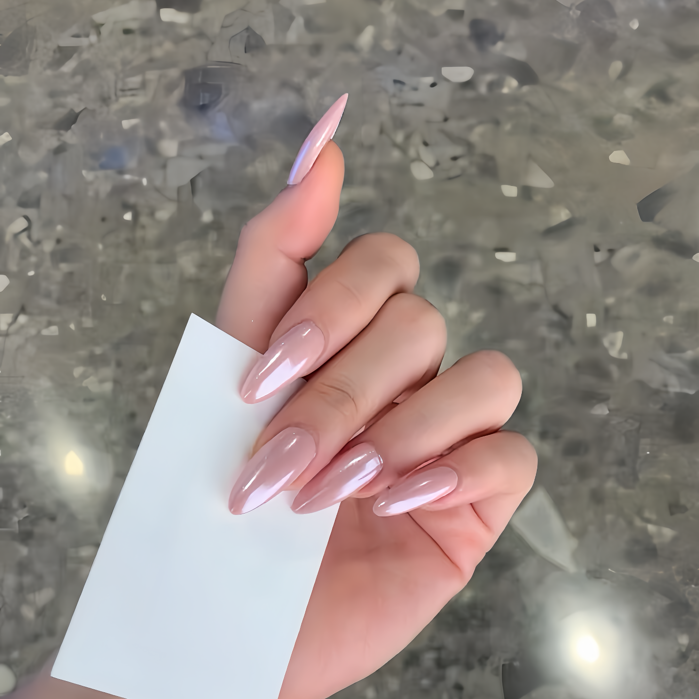 Hand with pink nail polish holding a white card against a reflective surface background