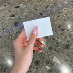 Hand holding a small white card against a textured concrete background