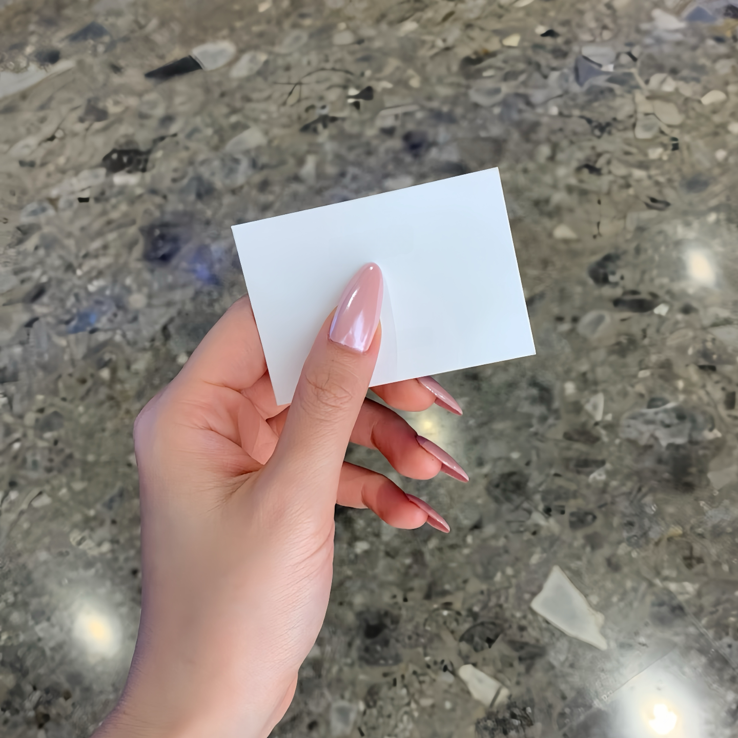 Hand holding a small white card against a textured concrete background