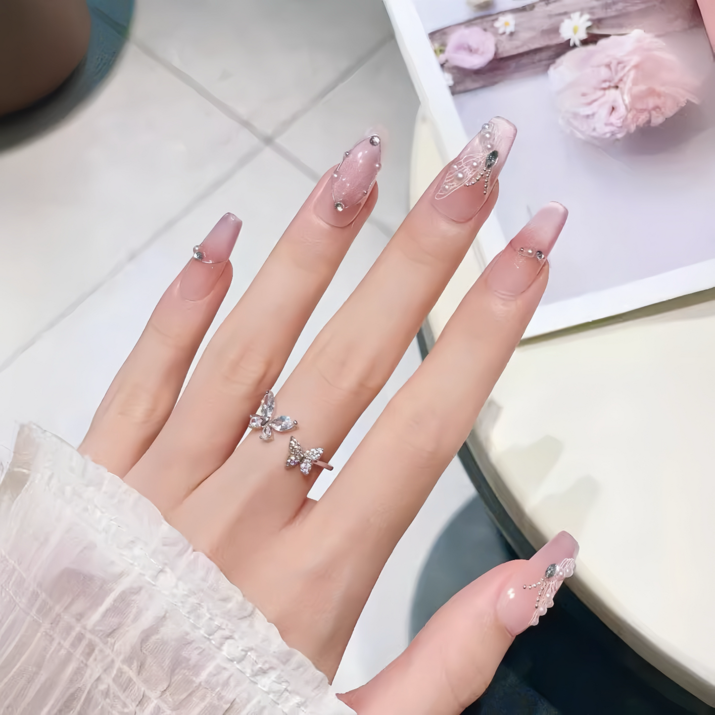 Hand with pink nail polish and butterfly rings on a light background