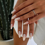 Close-up of hands with long, pointed nails holding a small white object against a blurred background.