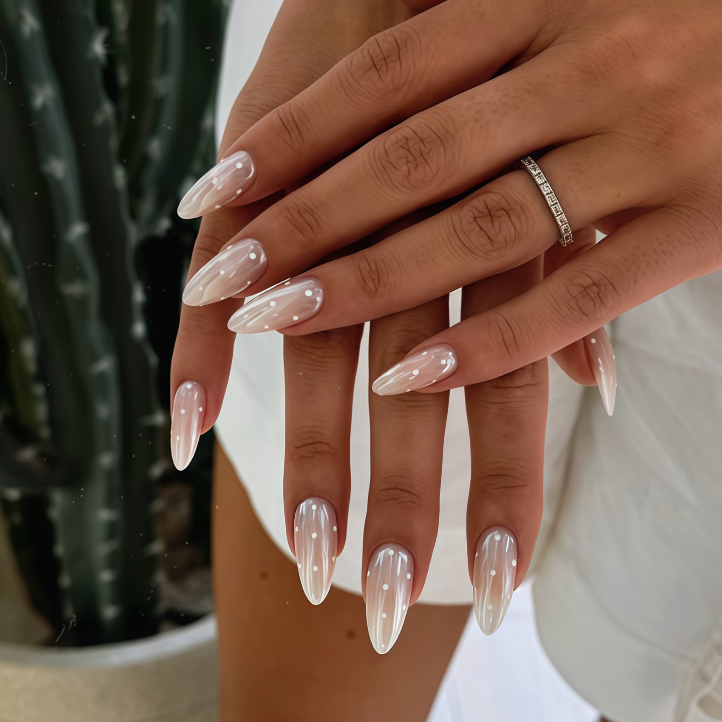 Close-up of hands with long, pointed nails holding a small white object against a blurred background.
