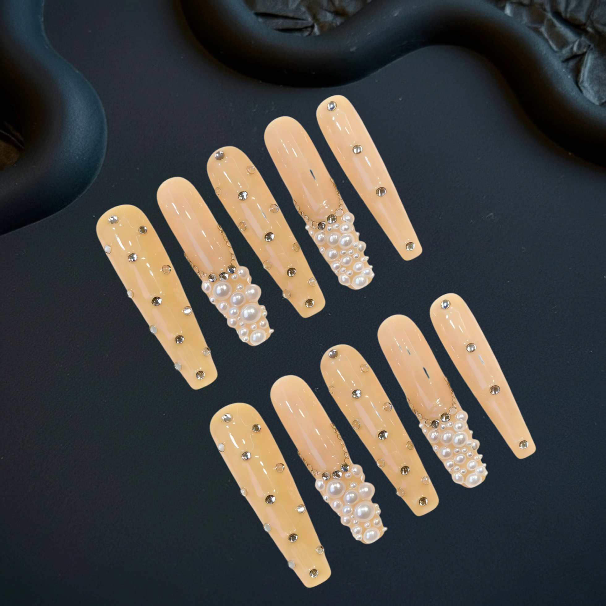 Set of beige false nails with pearls and rhinestones on a dark surface