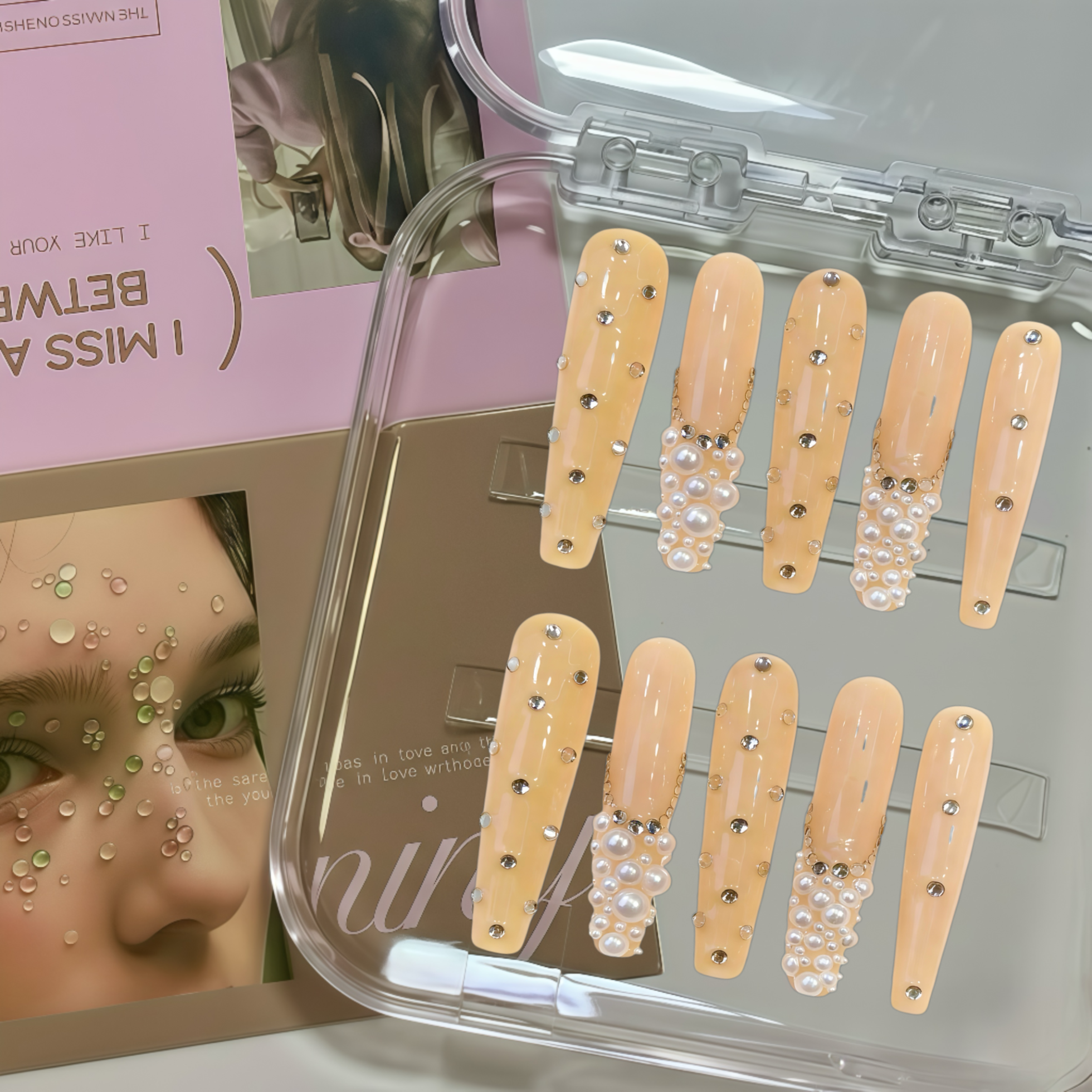Set of beige nail extensions with pearls and rhinestones in a clear case, with a magazine in the background.
