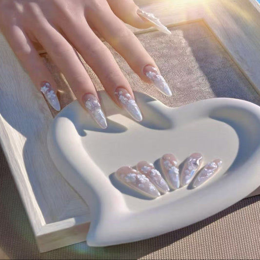 Heart-shaped dish with decorative items and a hand with glittery nails in the background