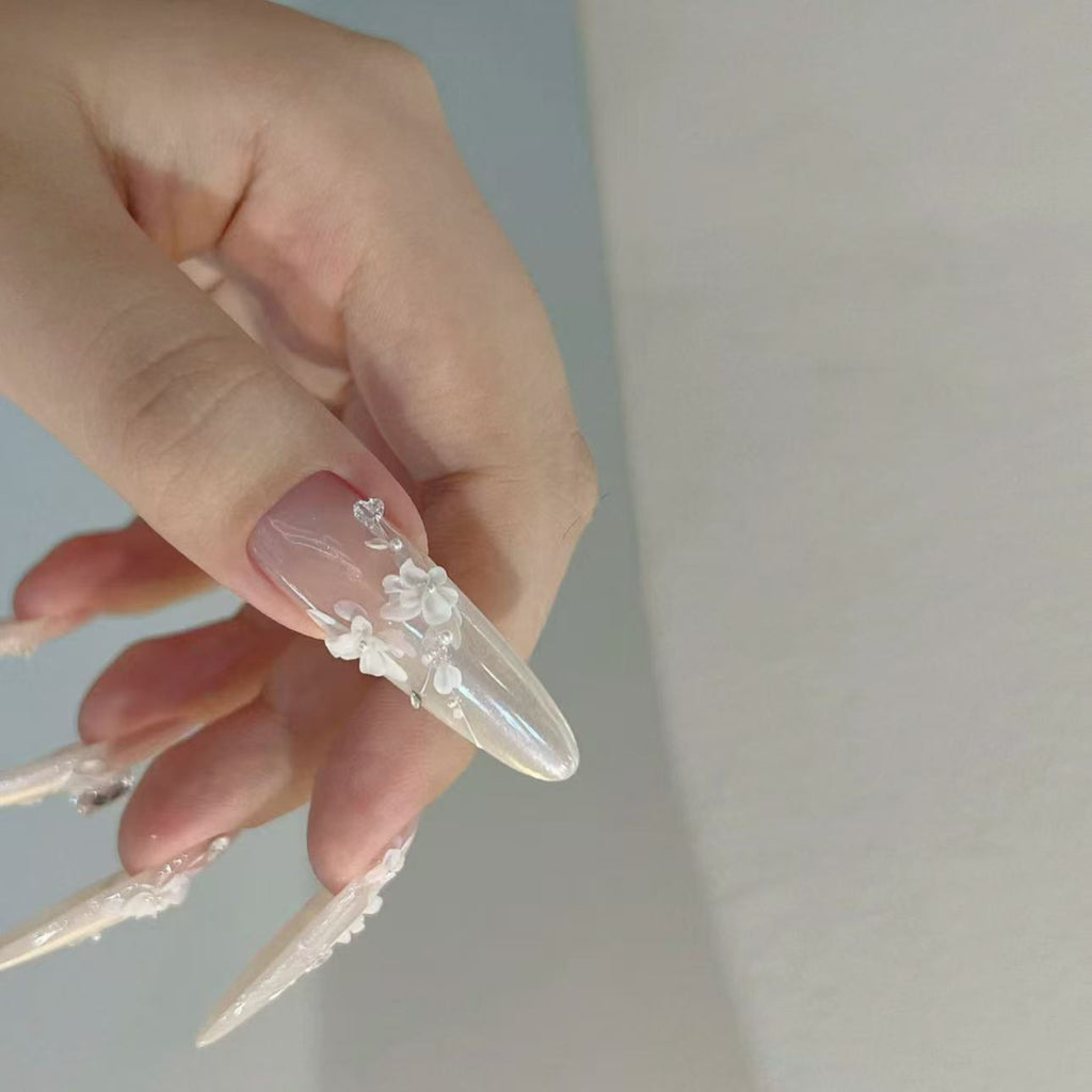 Hand with long, clear acrylic nails featuring floral designs on a plain background