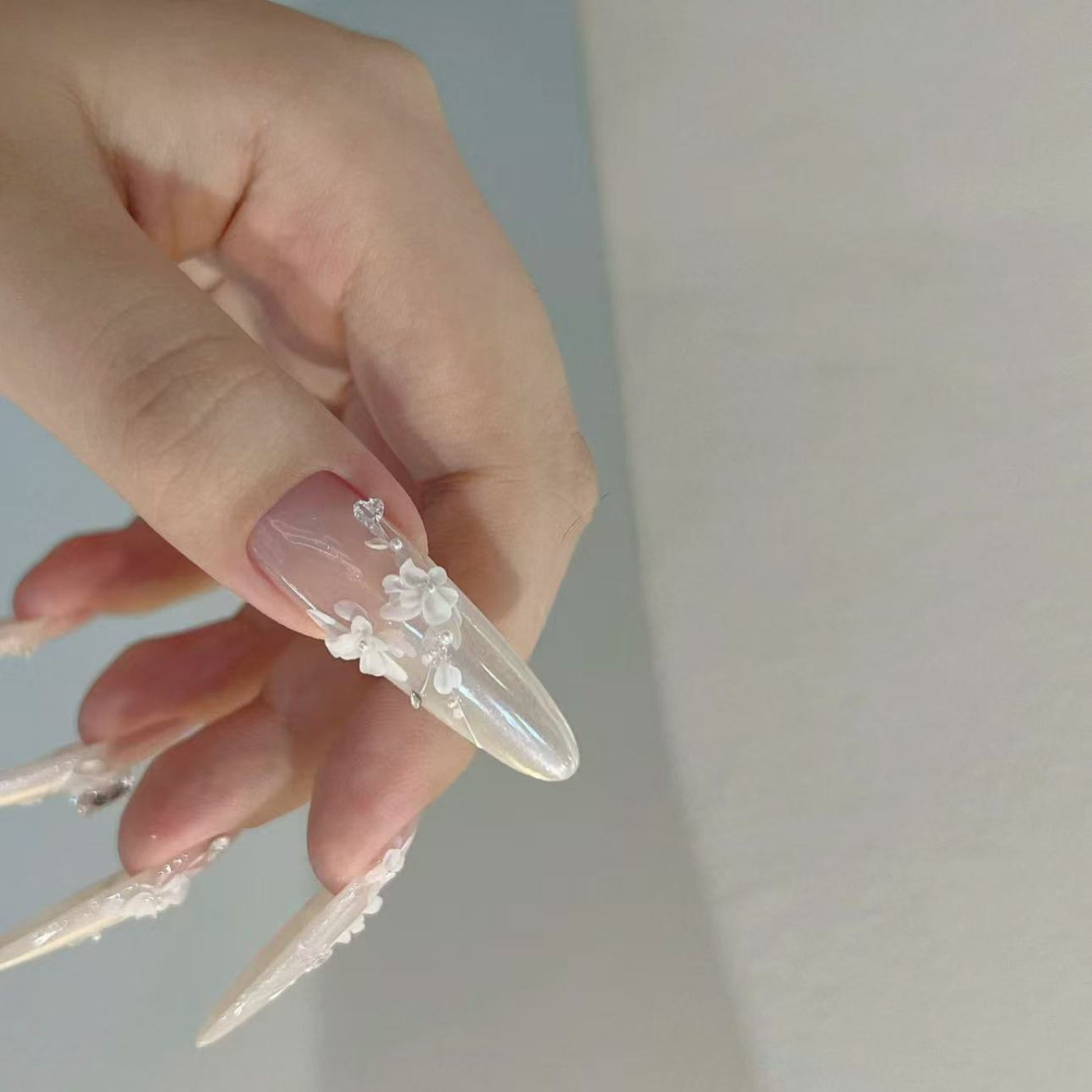 Hand with long, clear acrylic nails featuring floral designs on a plain background