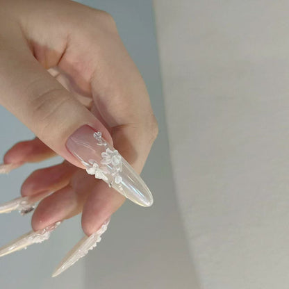 Hand with long, clear acrylic nails featuring floral designs on a plain background