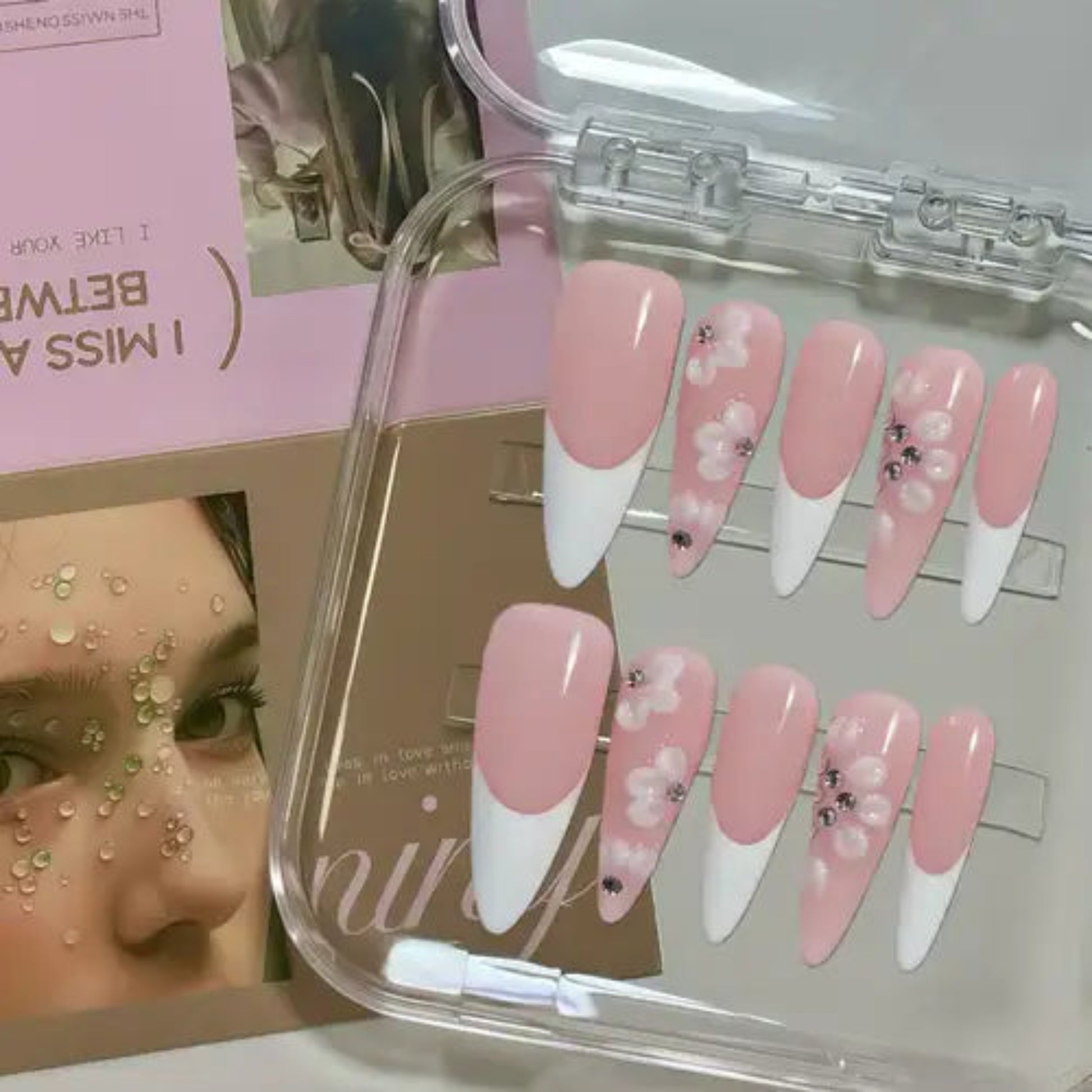 Set of pink and white nail extensions with decorative elements in a clear case.