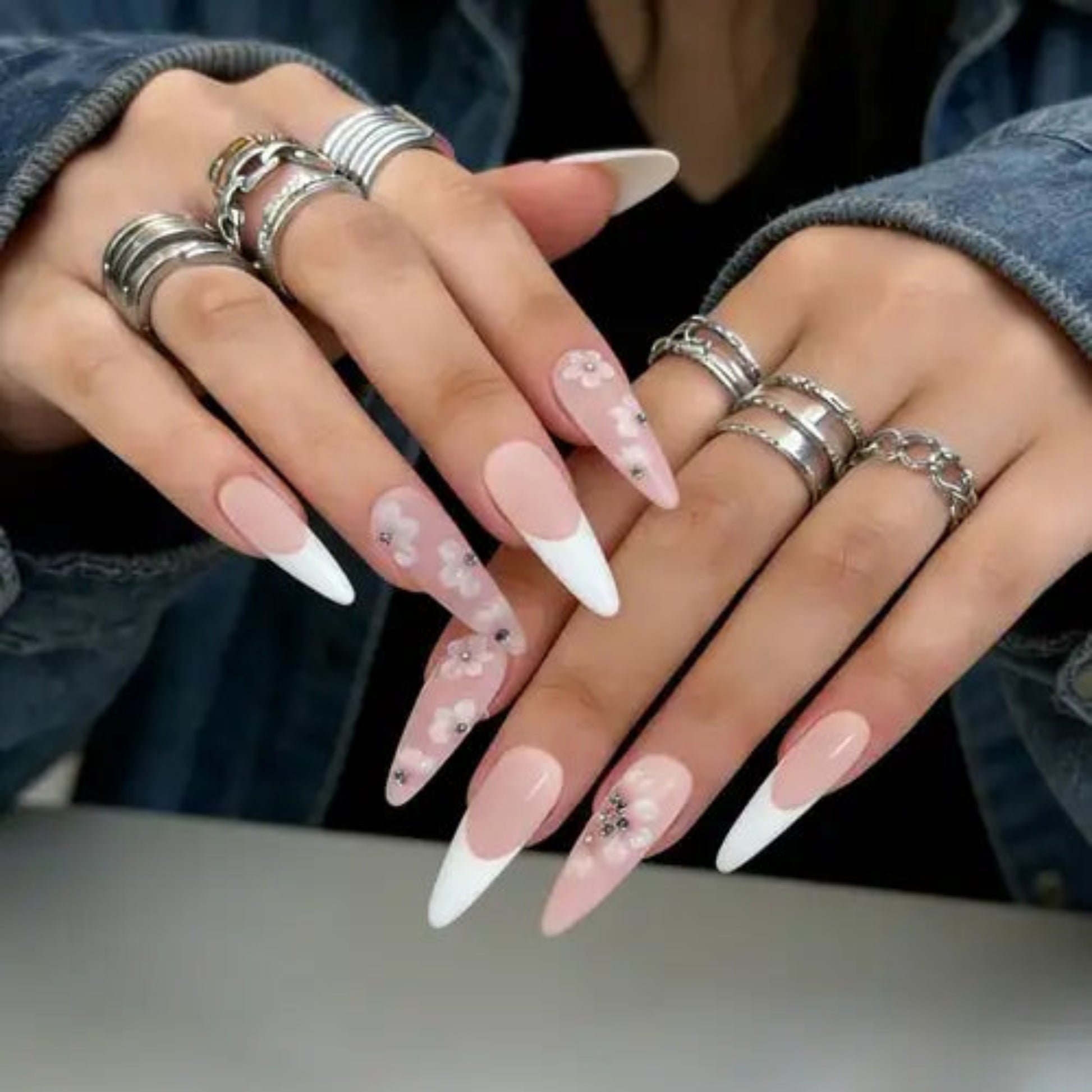 Close-up of hands with pink and white nail polish and multiple silver rings.