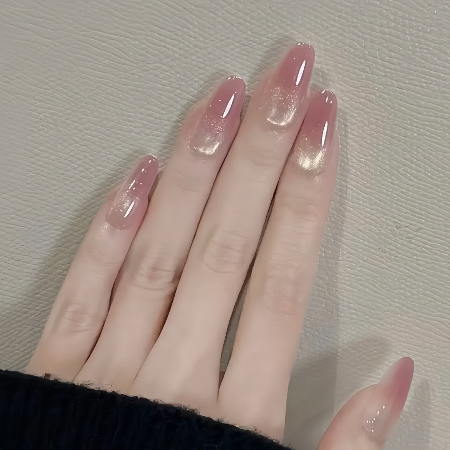 Hand with pink glittery nail polish on a neutral background