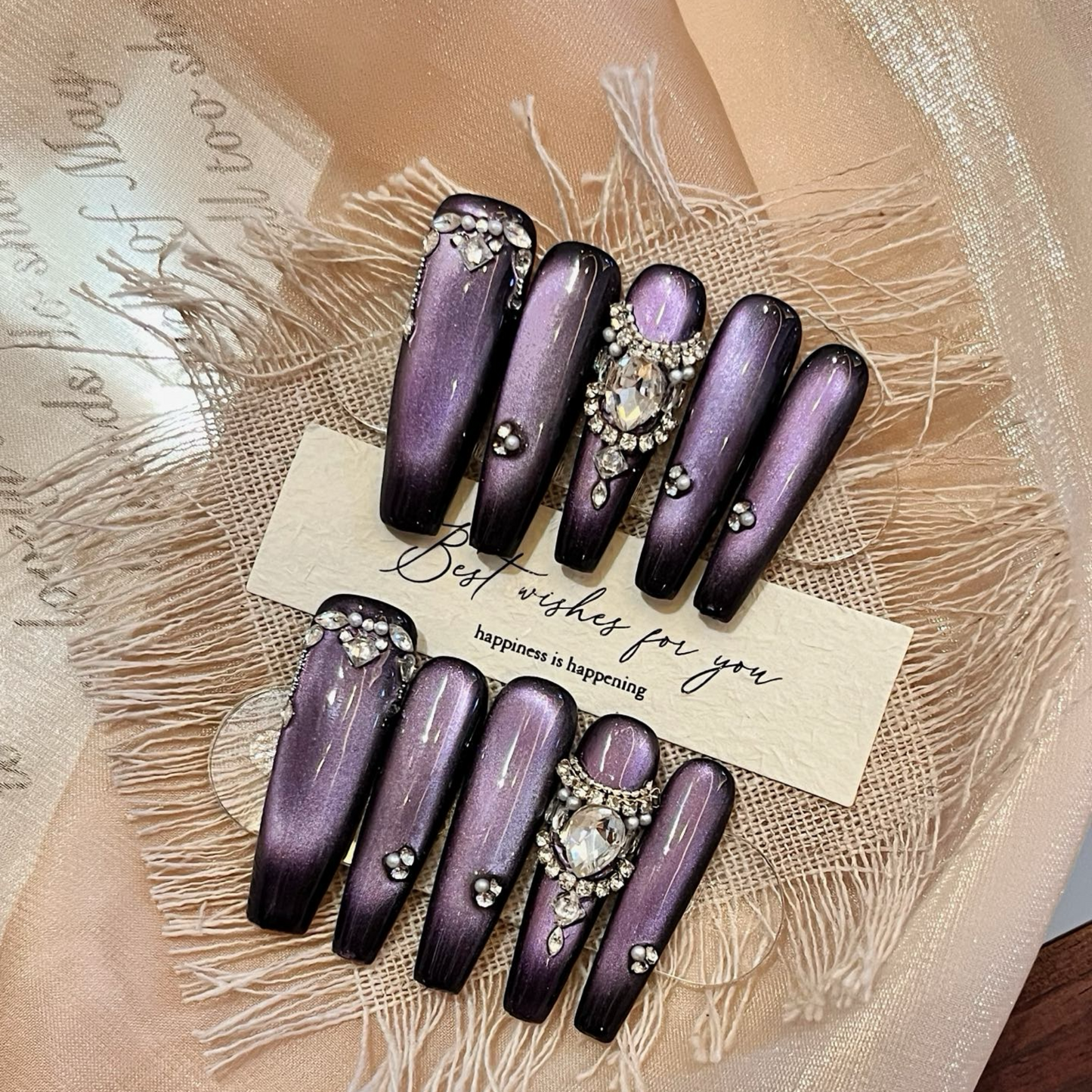 Purple nail art with rhinestones on a textured surface with a card.