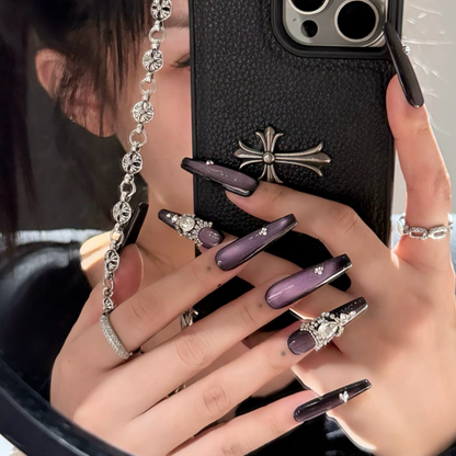 Person holding a phone with a black case featuring a cross design, wearing a ring and showing decorative nails.