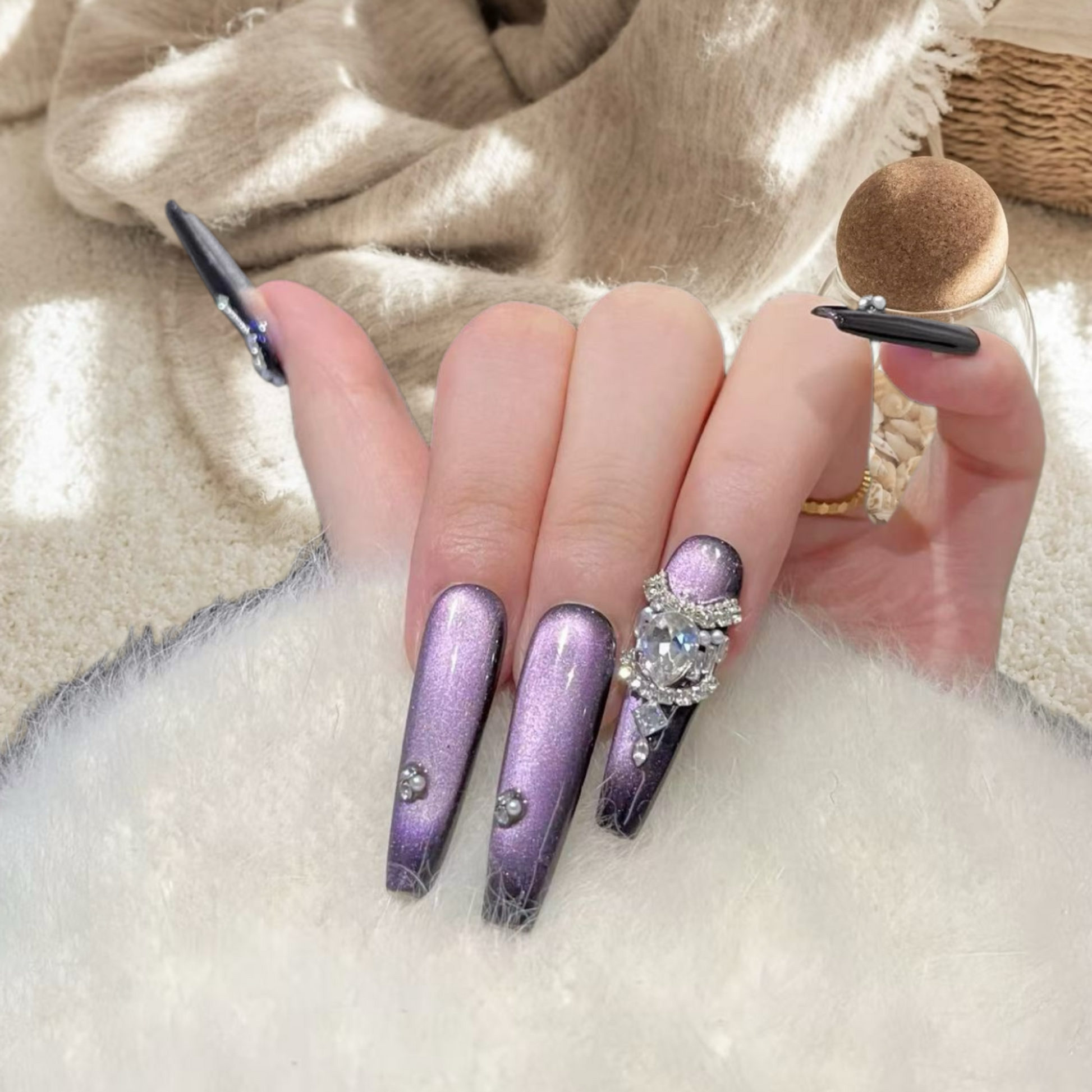 Hand with purple glittery nails and a diamond ring on a textured surface