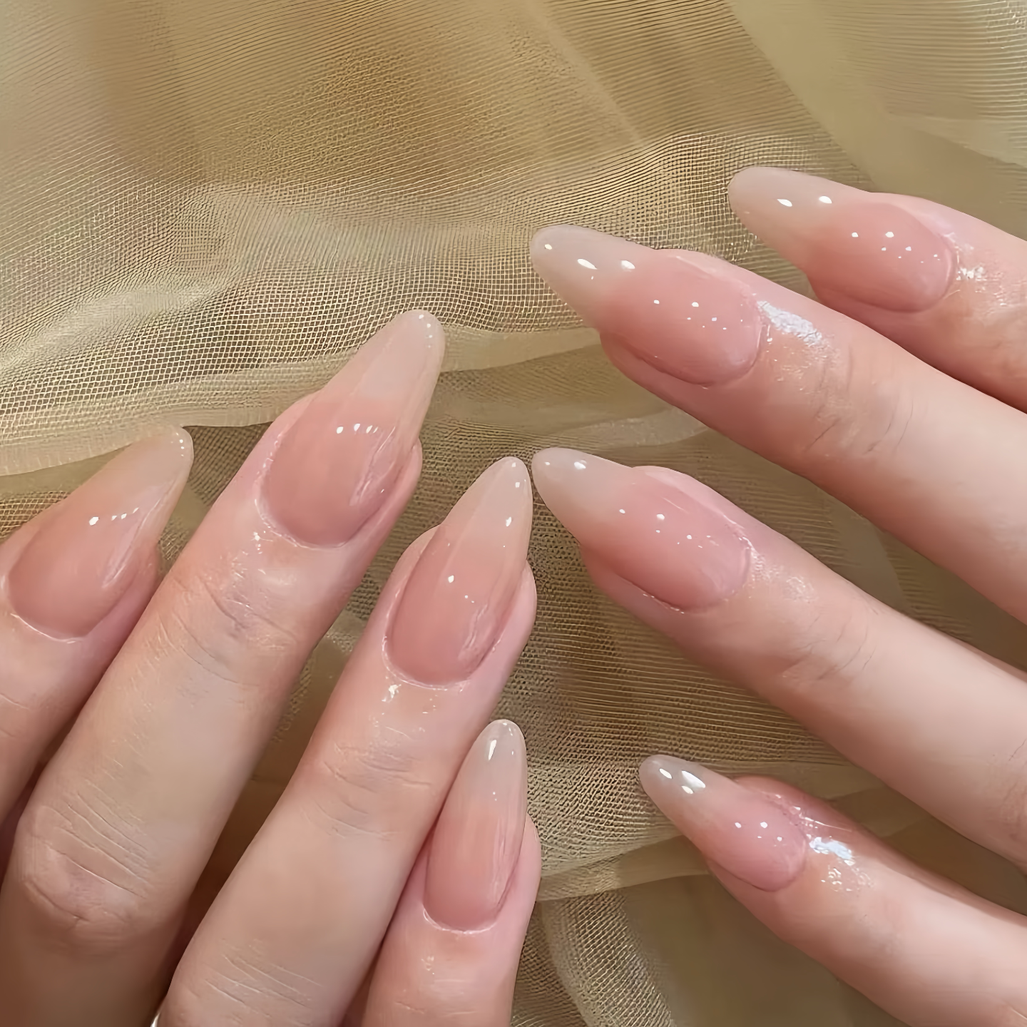 Close-up of hands with long, even pink nails against a beige fabric background