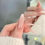 Close-up of hands with long, clear acrylic nails against a blurred background.