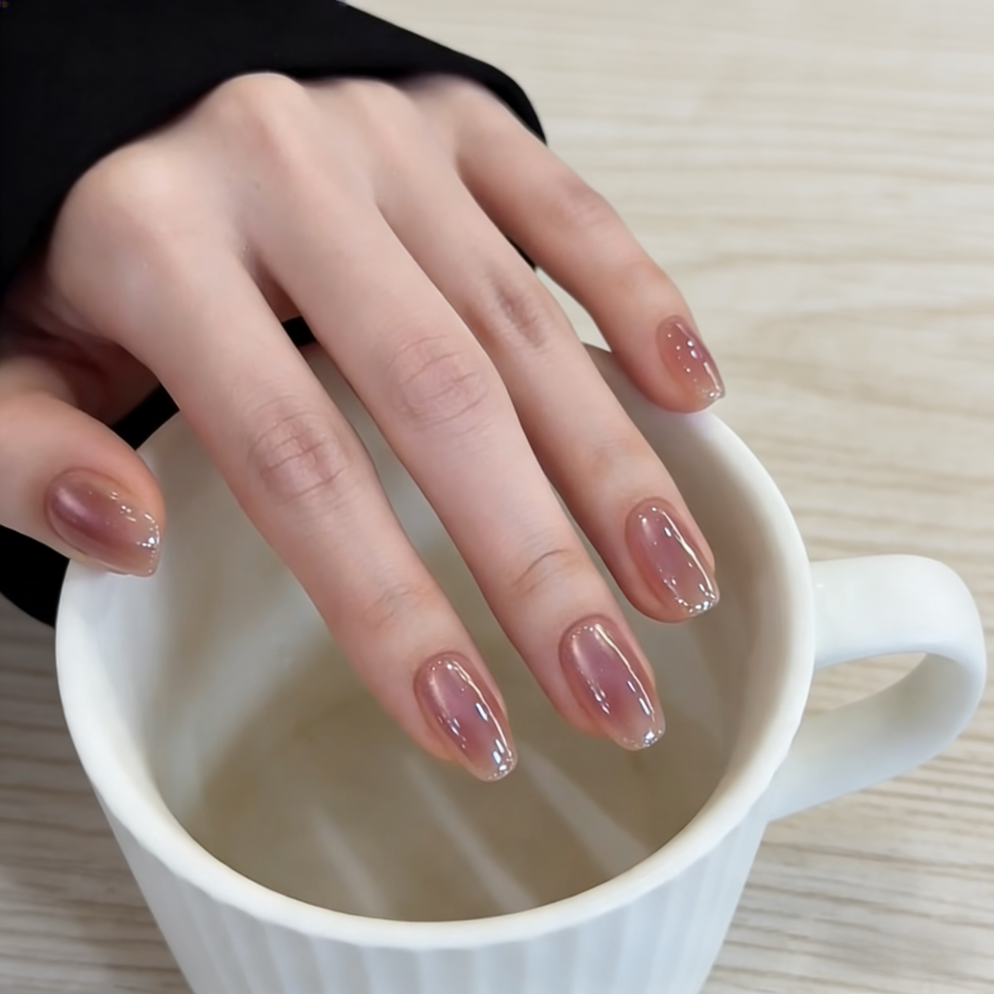 Hand with manicured nails holding a white mug on a light wooden surface