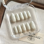 Set of light-colored false nails in a clear case on a textured surface.