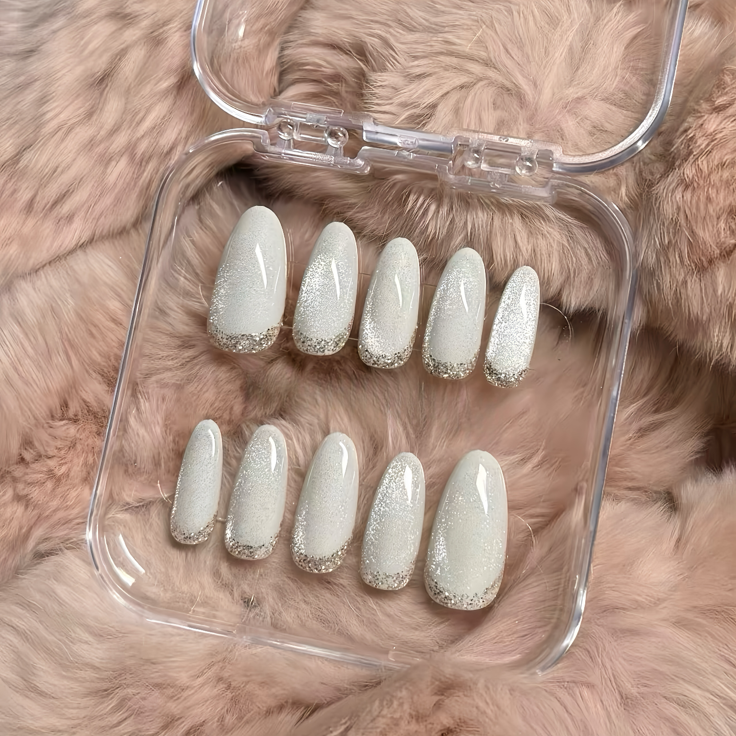 Set of white glittery nail extensions in a clear case on a fluffy pink surface
