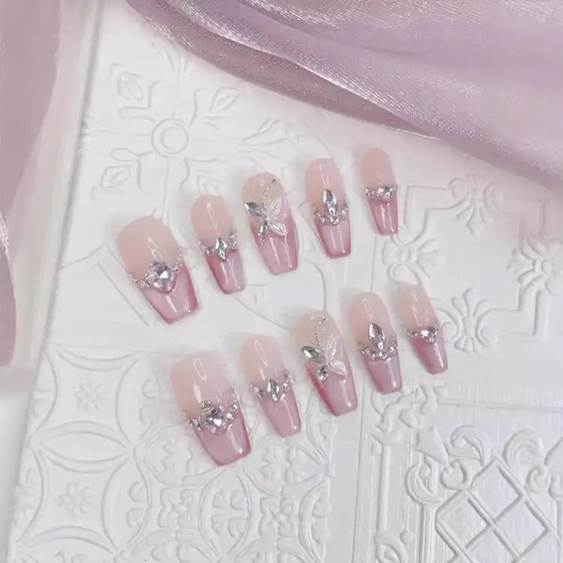 Set of pink nail designs with decorative elements on a textured white surface.